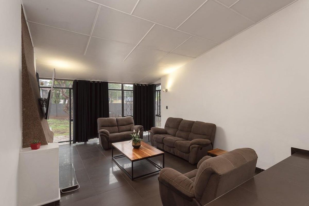 Spacious living room featuring large windows, tiled flooring, and a built-in fireplace, offering a bright and functional space for relaxation.
