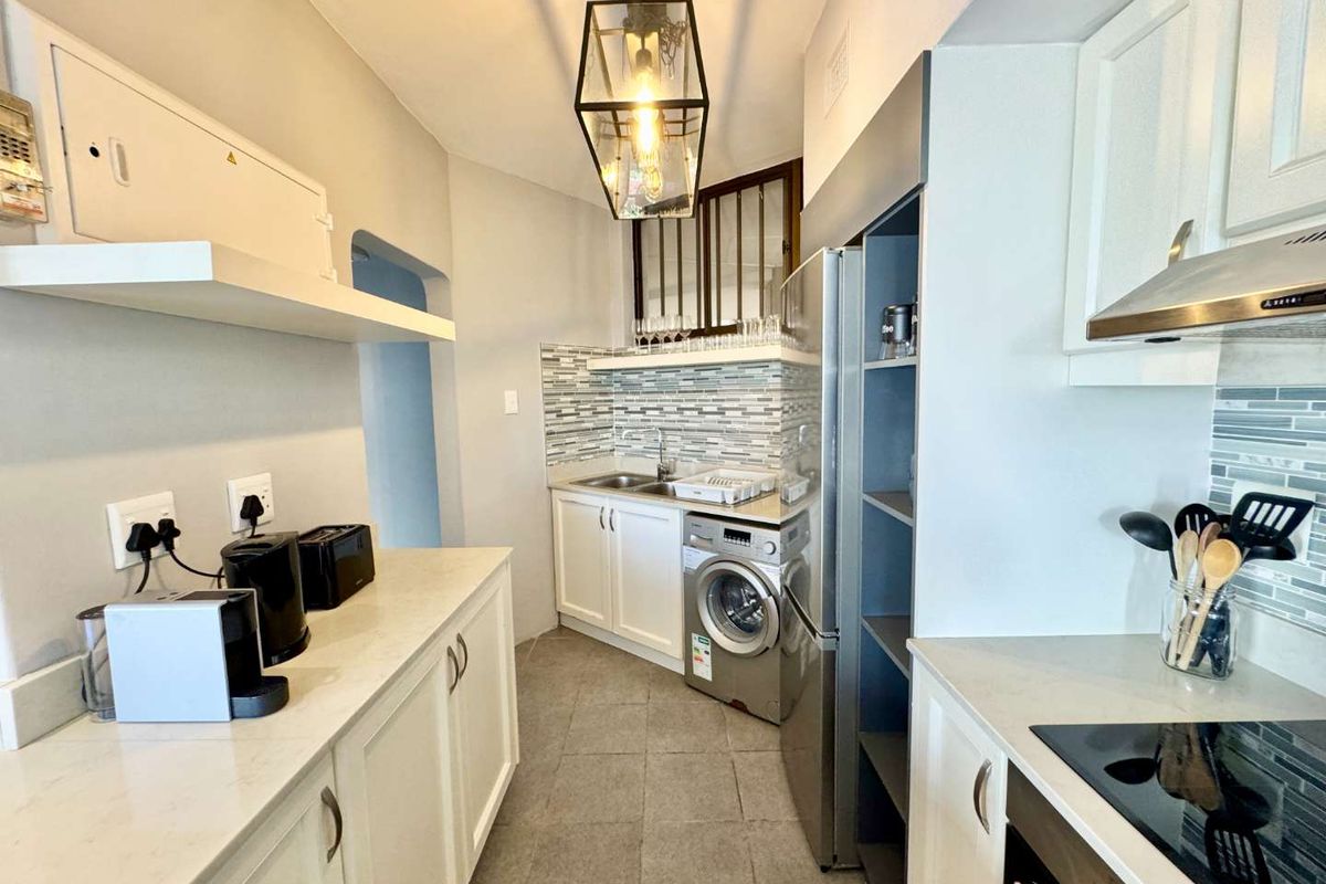Compact kitchen featuring white cabinetry, stone countertops, integrated stainless steel appliances, and a tiled backsplash with a modern pendant light fixture.