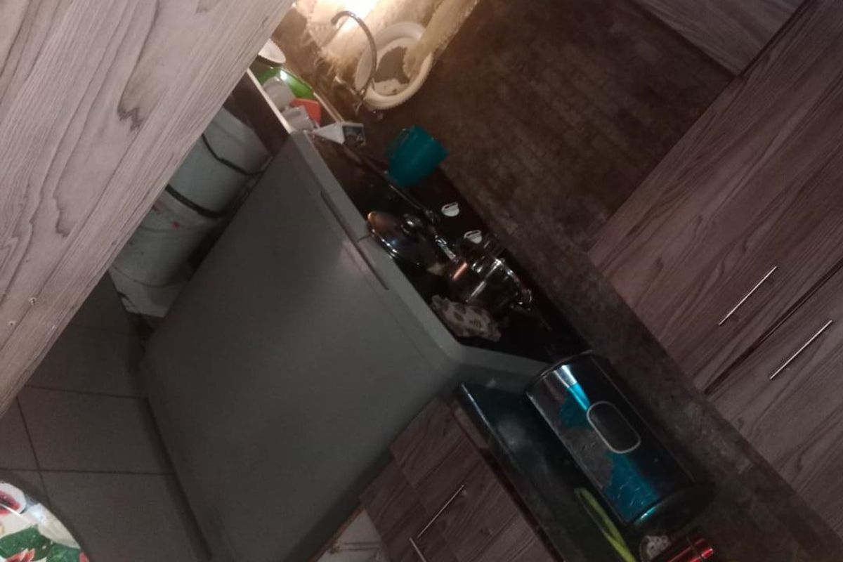 A compact kitchen featuring wood-grain cabinetry, tiled backsplash, and a stainless steel sink, currently showing signs of wear and missing cabinet components.