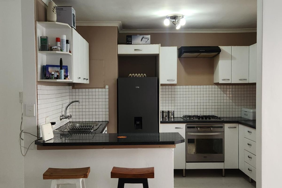 A functional kitchen featuring white cabinetry, granite countertops, a gas hob, built-in oven, and a tiled backsplash with a breakfast bar area.