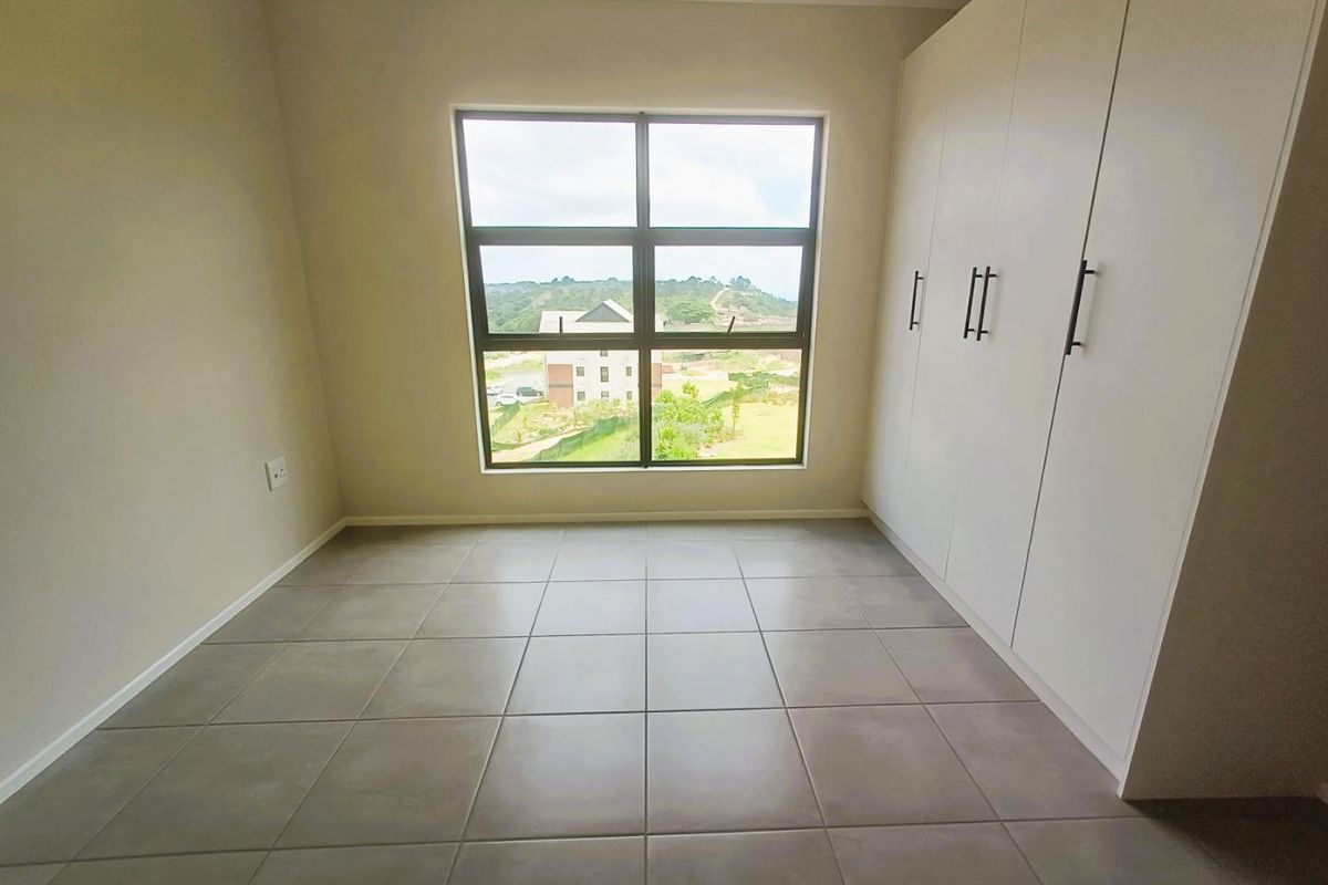 A bright, empty bedroom featuring neutral floor tiles, built-in cupboards, and a large window offering scenic views.