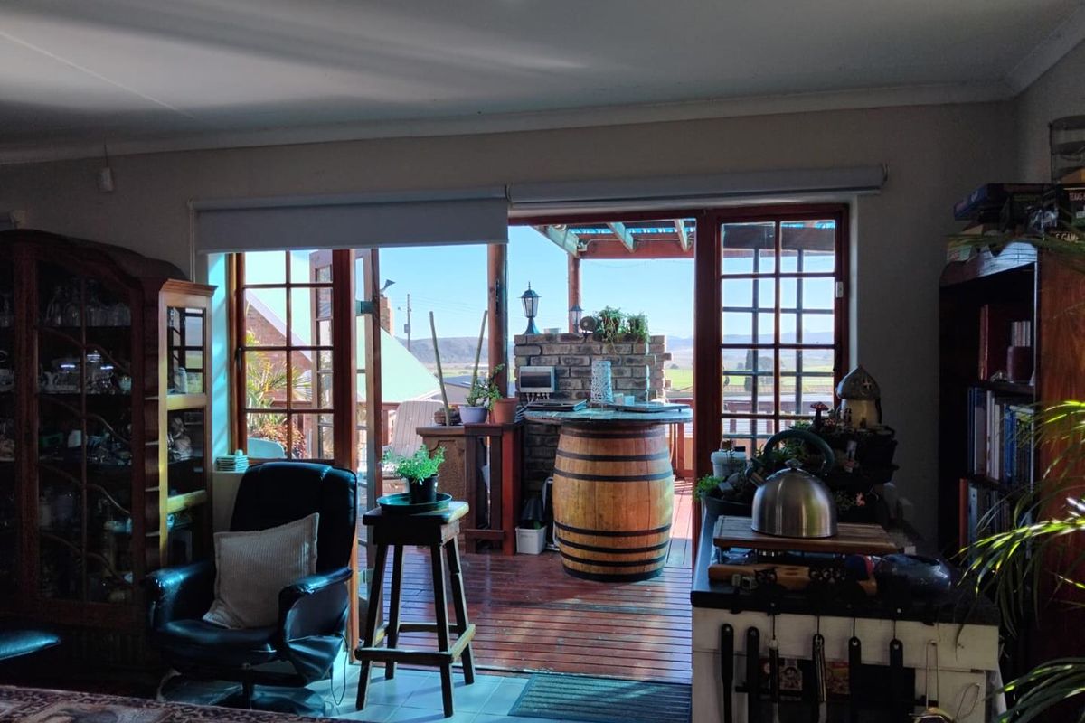 A living area featuring large wooden framed glass doors that open onto a covered outdoor patio with a brick built-in braai area.