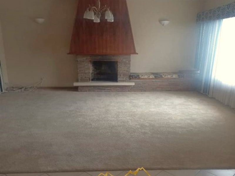 Spacious living room featuring a prominent fireplace with stone detailing, built-in bench seating, and a combination of tiled and carpeted flooring.