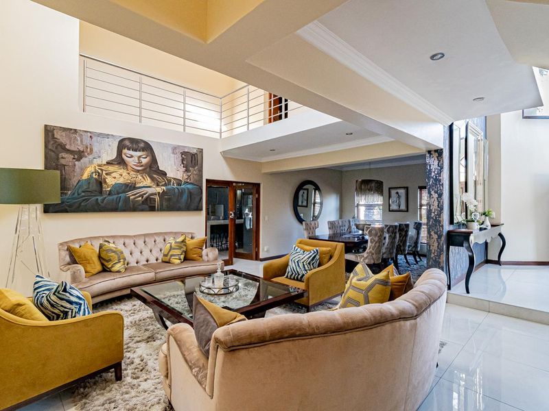 Spacious open-plan living and dining area featuring double-volume ceilings, a mezzanine level with modern balustrades, and polished tiled flooring throughout.