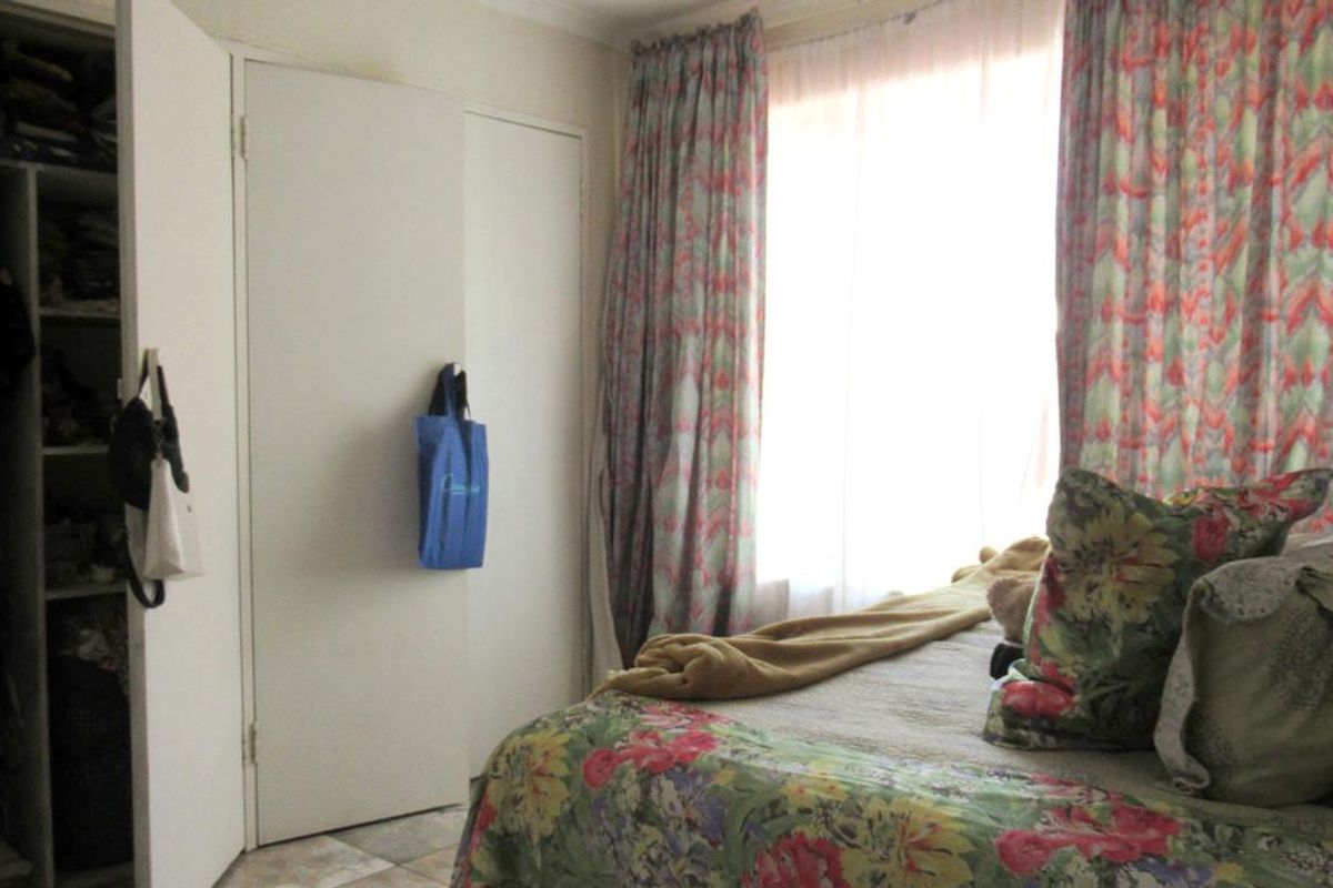 A bedroom featuring built-in cupboards with shelving and a window dressed with patterned curtains.