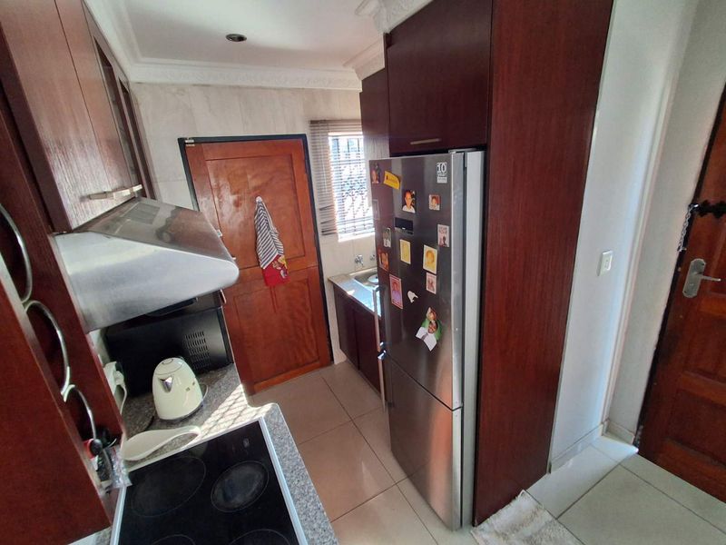 A compact kitchen featuring dark wood cabinetry, granite countertops, an electric hob, and an integrated extractor fan with tiled flooring throughout.