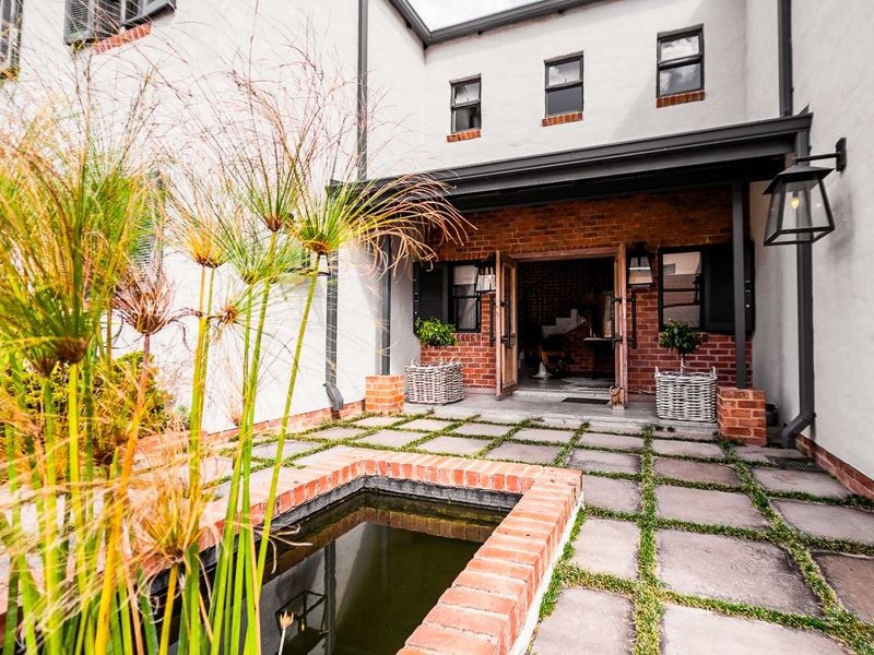 A charming rear courtyard featuring a stone-paved patio, a built-in brick water feature, and a covered entrance with double doors.