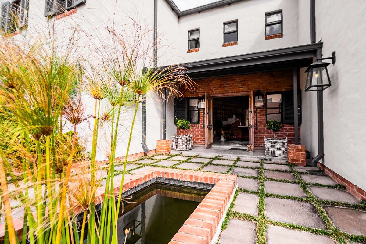A charming rear courtyard featuring a stone-paved patio, a built-in brick water feature, and a covered entrance with double doors.