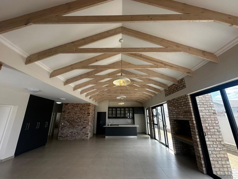 Spacious open-plan living area featuring a vaulted ceiling with exposed timber trusses, brick feature walls, a modern kitchen island, and large sliding doors.