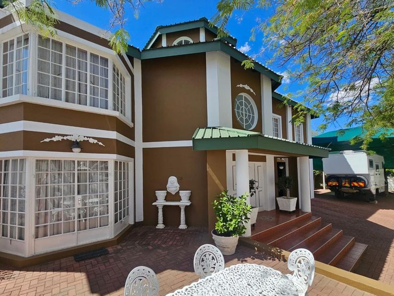 Front elevation of a multi-story house featuring a covered entrance porch, brick paved driveway, bay windows, and a distinctive circular architectural window.