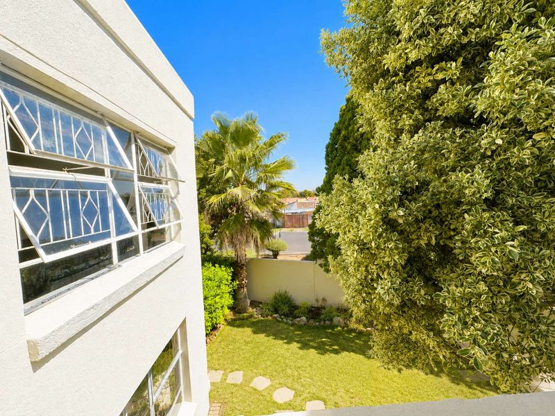 A view of the rear garden and boundary wall from an elevated position, featuring established trees and white exterior building facade with louvre windows.