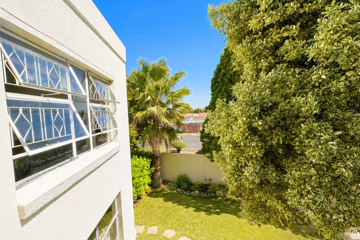 A view of the rear garden and boundary wall from an elevated position, featuring established trees and white exterior building facade with louvre windows.