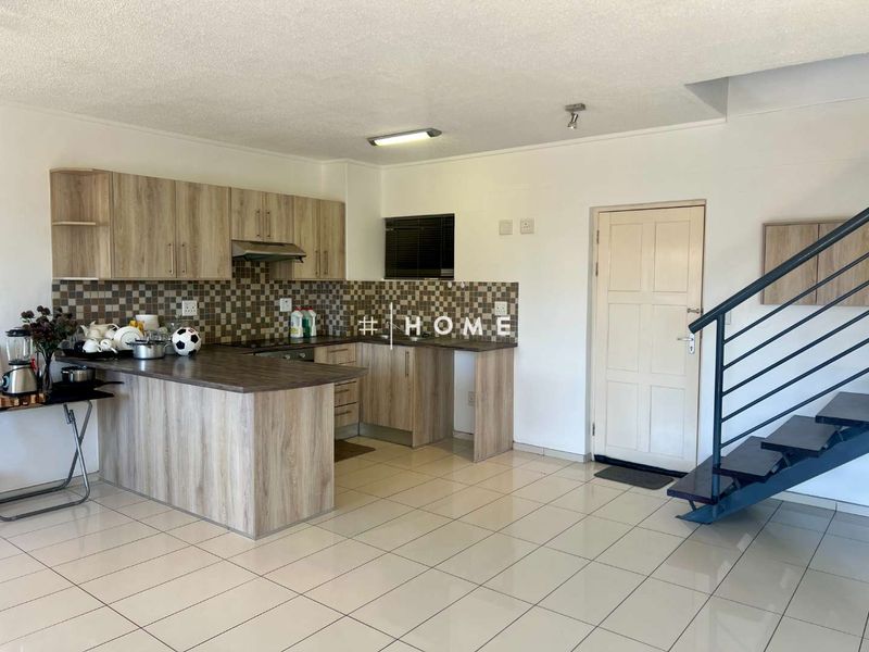 Open plan kitchen featuring laminate cabinetry, tiled backsplash, and tiled flooring, adjacent to a staircase leading to the upper level.