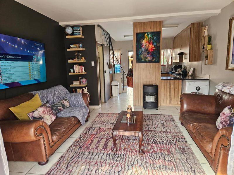 Open-plan living area featuring tiled flooring, a compact kitchen with wood-finish cabinetry, and a staircase leading to the upper level.
