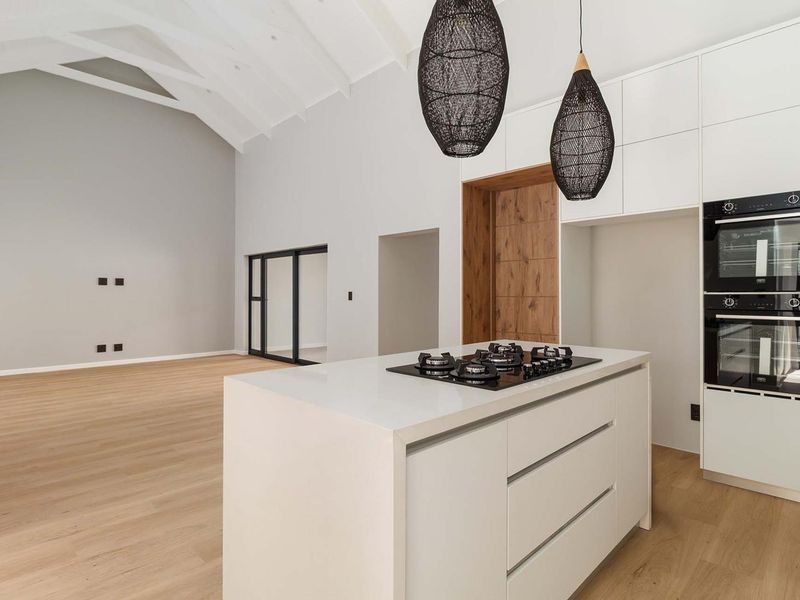 Spacious open-plan living area featuring a modern kitchen with a central island, gas cooktop, double ovens, and high vaulted ceilings with timber flooring.