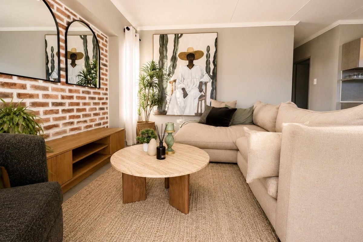 A well-presented living room featuring a decorative exposed brick feature wall, recessed downlighting, and neutral finishes throughout.