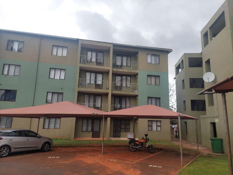Exterior view of a multi-story apartment complex featuring balconies, dedicated carport parking, and paved common areas.