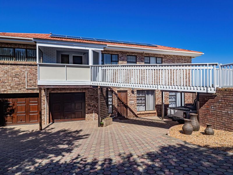 Front elevation of a double-story brick house featuring a paved driveway, double garage, and an elevated wooden deck balcony with solar panels on the roof.