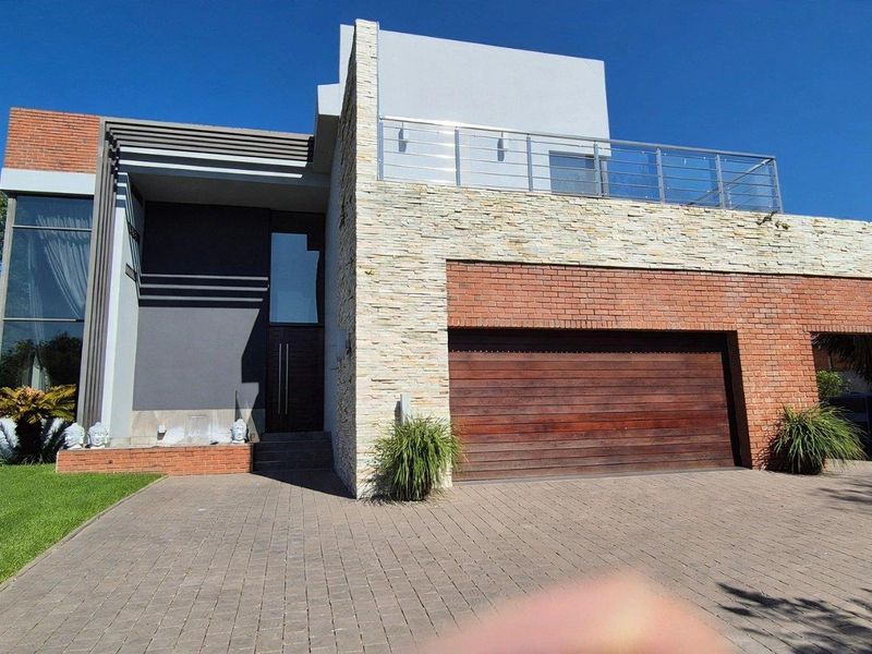 Modern double-story residence featuring a striking combination of stone cladding and brickwork, complete with a spacious paved driveway and an upper-level balcony.