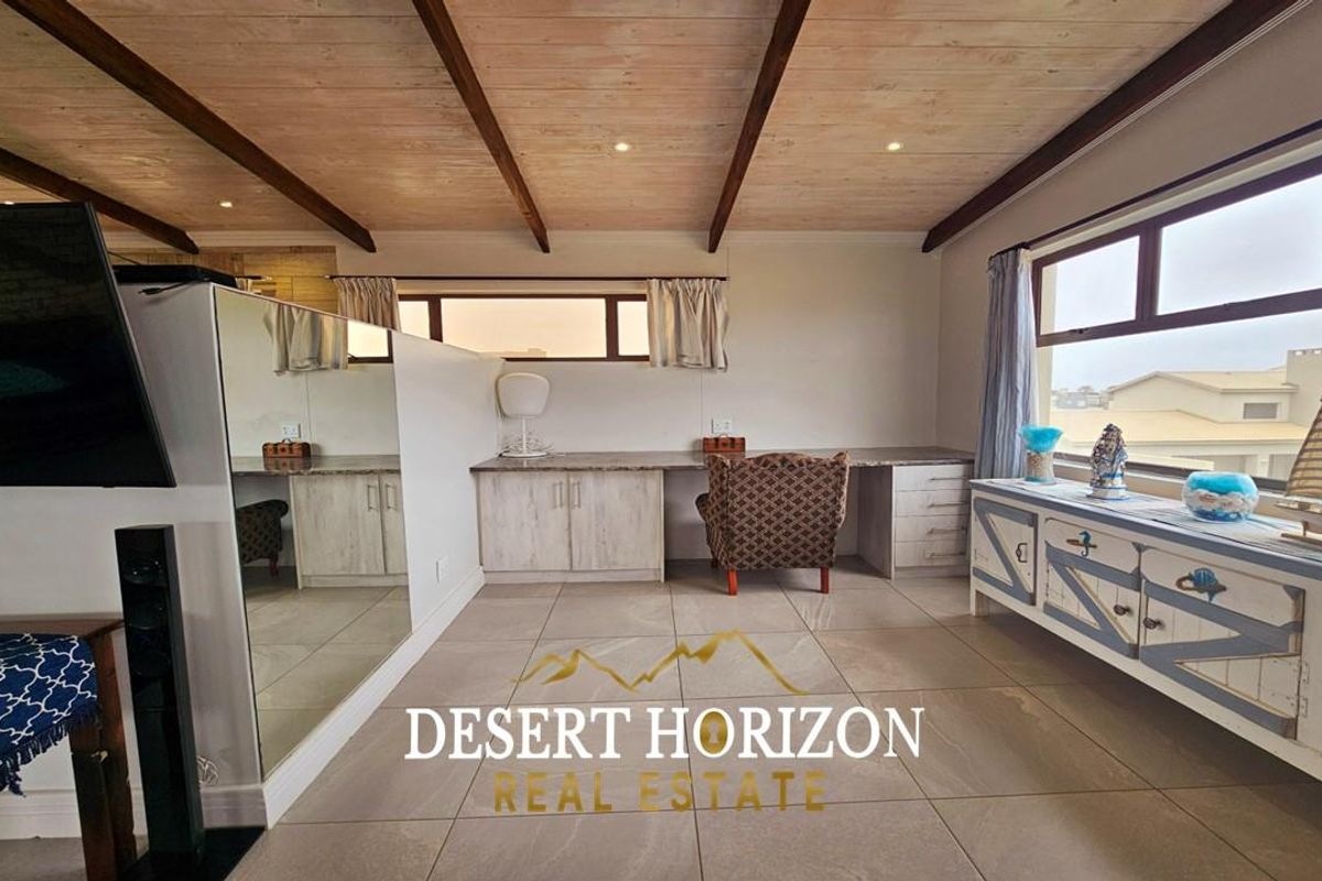 A bright living area featuring a built-in desk, tiled flooring, and a timber-paneled ceiling with exposed beams.
