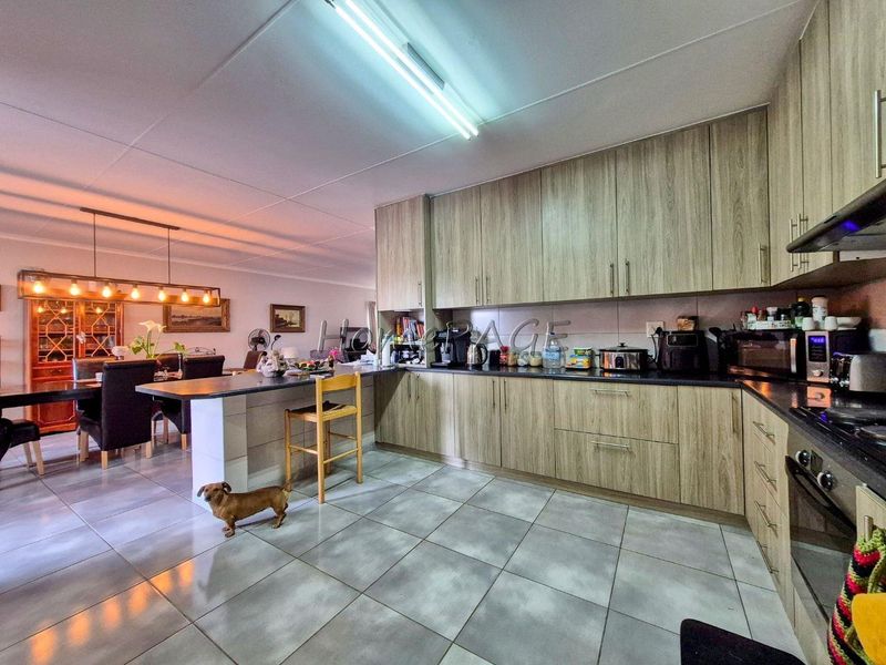 Open-plan kitchen and dining area featuring modern wood-look cabinetry, dark countertops, tiled flooring, and a functional breakfast bar layout.