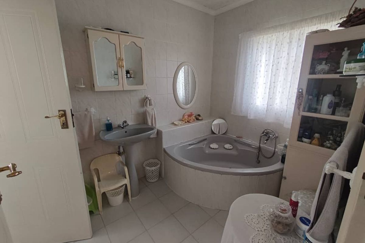 A functional bathroom featuring a corner bathtub, pedestal basin, and wall-mounted medicine cabinet with tiled walls and flooring.
