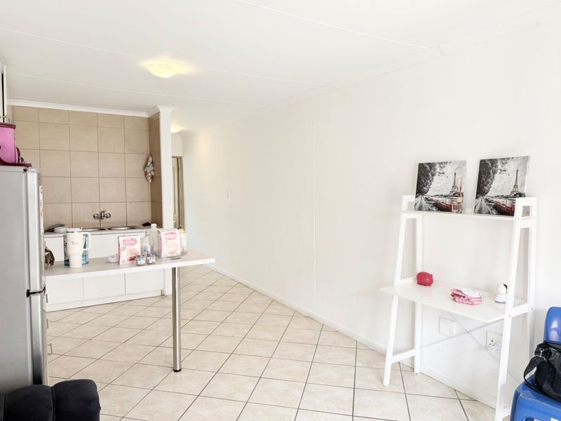 Open plan living area featuring a functional kitchen with tiled splashback, breakfast bar, and neutral tiled flooring throughout the space.