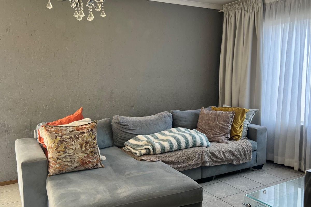 A living room featuring tiled flooring and a large window with curtains, providing a neutral space for relaxation.