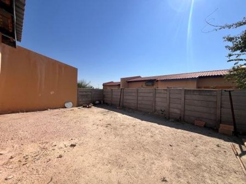 A spacious, unlandscaped rear yard area enclosed by precast concrete boundary walls, offering potential for garden development or outdoor improvement.