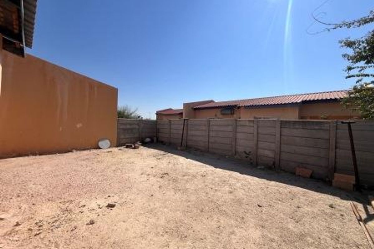 A spacious, unlandscaped rear yard area enclosed by precast concrete boundary walls, offering potential for garden development or outdoor improvement.