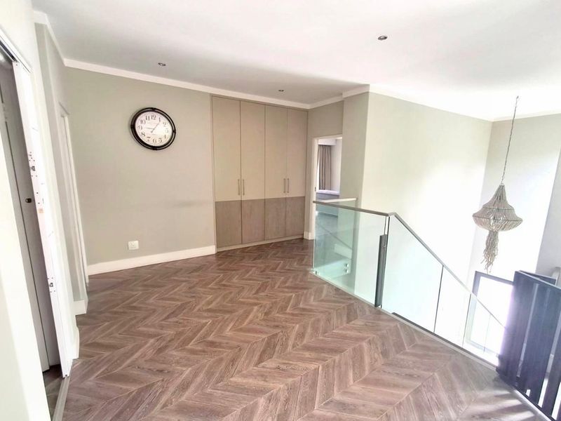 A bright and modern landing area featuring high-quality herringbone flooring, built-in storage cupboards, and a contemporary glass balustrade overlooking the staircase.