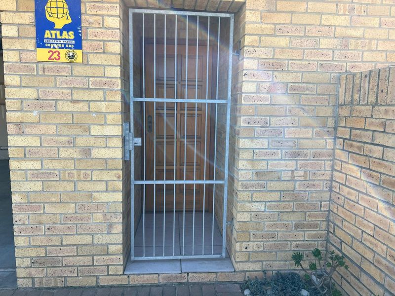 Main entrance featuring a secure metal gate and a solid timber front door set within a facebrick facade.
