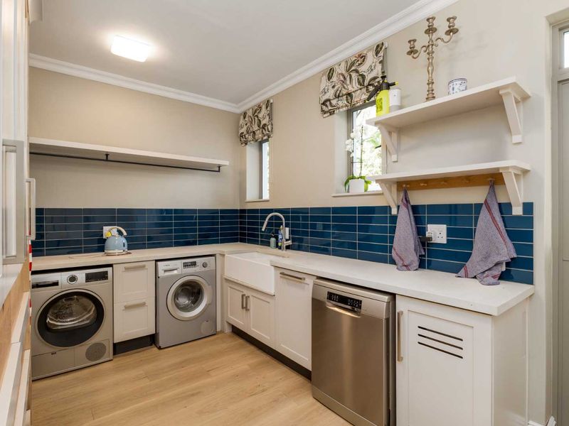 A well-appointed laundry room featuring a farmhouse sink, blue subway tile backsplash, stone countertops, and ample built-in cabinetry with integrated dishwasher.