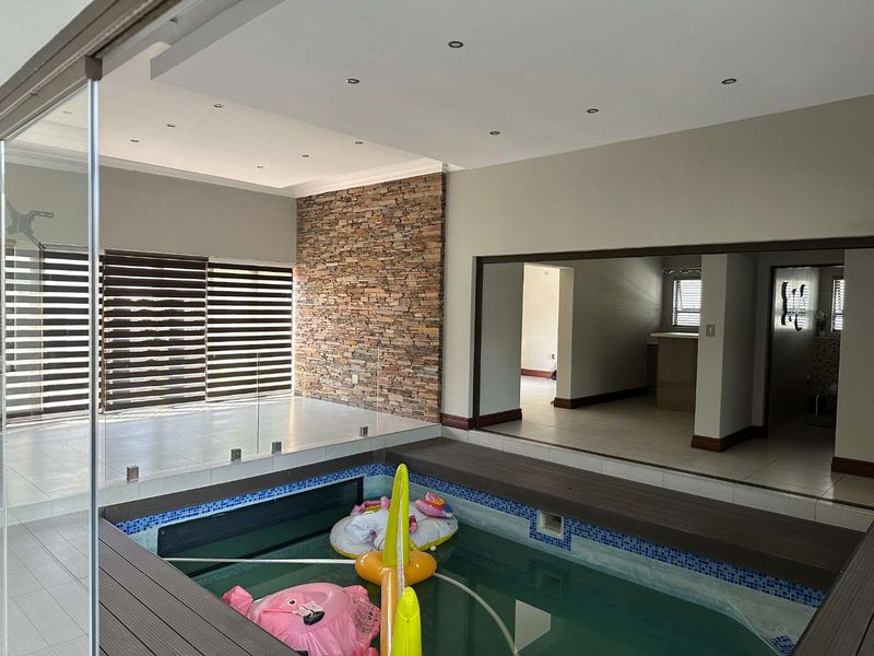 Indoor swimming pool area featuring a stone accent wall, tiled flooring, and glass balustrade, seamlessly integrated into the living space.