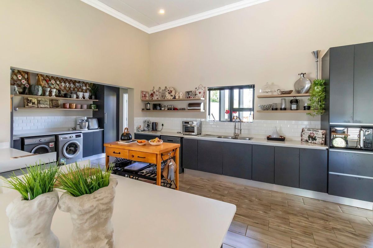 Modern kitchen featuring dark cabinetry, white subway tile backsplash, integrated appliances, and an adjoining scullery area with laundry facilities.