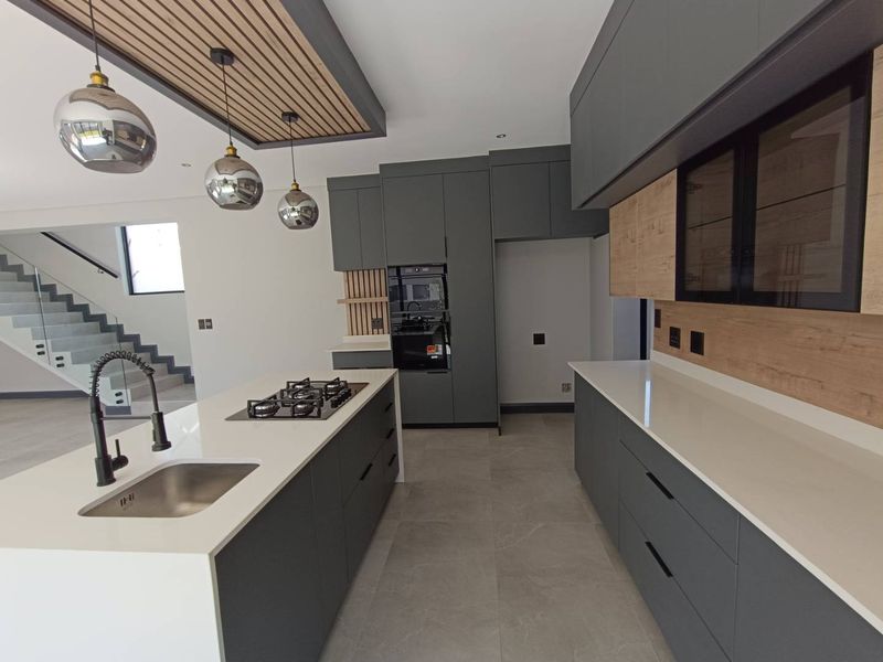 Modern kitchen featuring a central island with gas hob, quartz countertops, sleek cabinetry, and a stylish slatted timber ceiling detail.