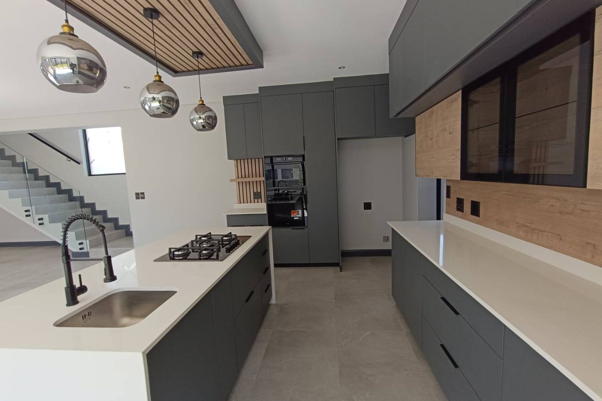 Modern kitchen featuring a central island with gas hob, quartz countertops, sleek cabinetry, and a stylish slatted timber ceiling detail.