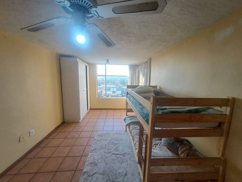 A bedroom featuring tiled flooring, a ceiling fan, and a built-in wardrobe, offering a functional space with potential for cosmetic updates.