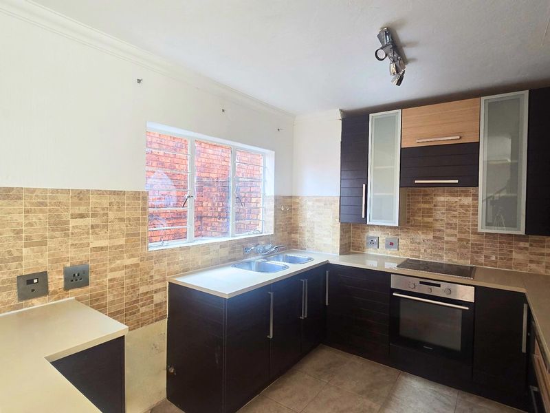 Modern kitchen featuring dark cabinetry, light countertops, tiled backsplash, and integrated oven and hob, offering a clean and functional workspace.
