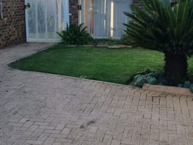 A rear exterior view featuring a thatched roof structure, brick paved courtyard, and established garden area.