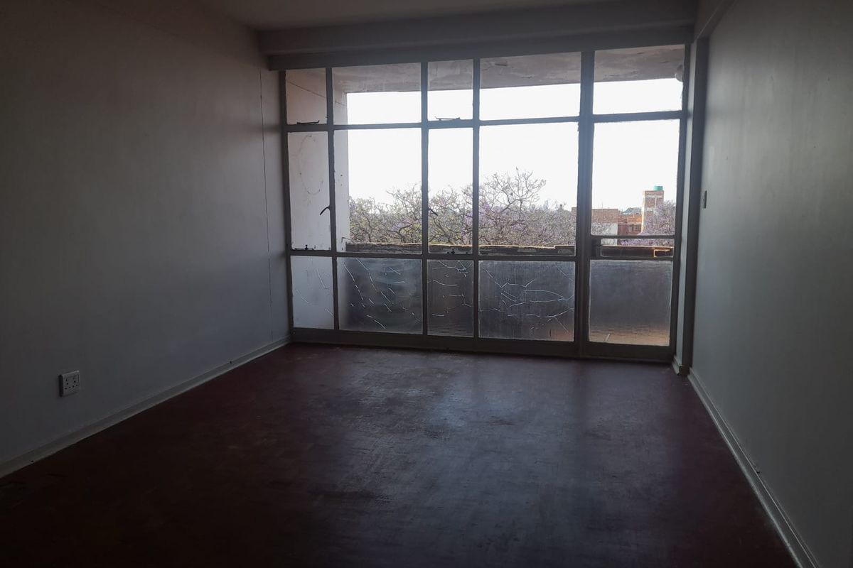 An empty living room featuring a large metal-framed window with cracked glass and access to a balcony, requiring renovation and cosmetic updates.