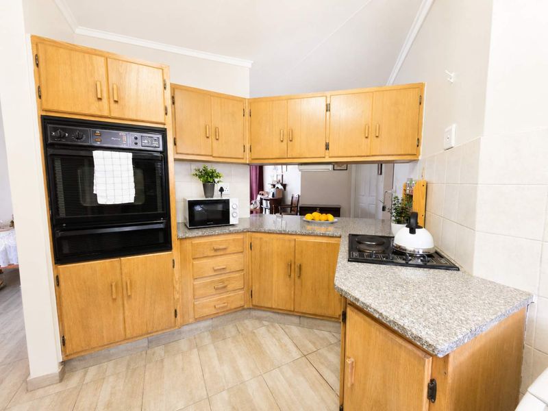 A functional kitchen featuring wooden cabinetry, granite countertops, a built-in oven, and a hob, with tiled flooring and a neutral tiled backsplash.