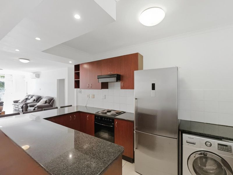 Open-plan kitchen featuring dark granite countertops, wood-finish cabinetry, and integrated appliances, flowing seamlessly into the adjacent living area.