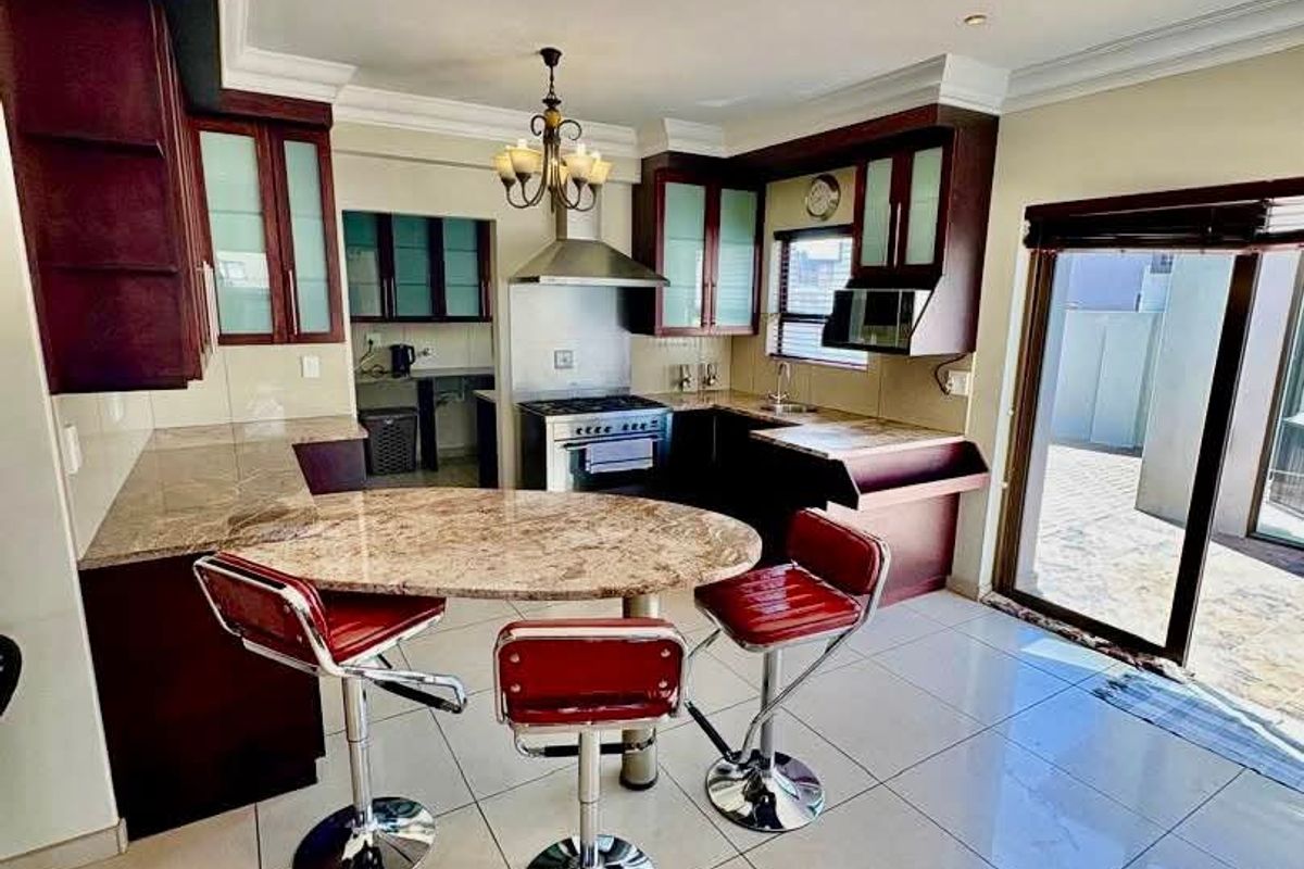 A kitchen featuring dark wood cabinetry, granite countertops, a built-in oven with extractor fan, and tiled flooring with direct access to an outdoor patio area.