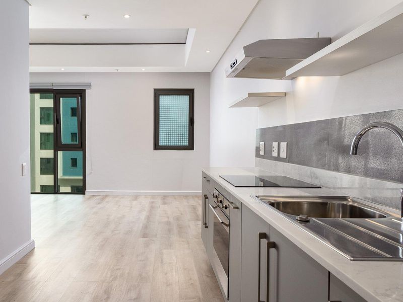 Modern open-plan kitchen and living area featuring sleek grey cabinetry, integrated appliances, light wood-look flooring, and access to a balcony.