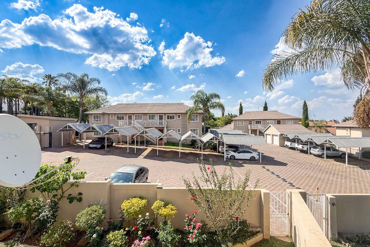 An elevated view of an apartment complex featuring paved parking areas with covered carports and landscaped garden beds.