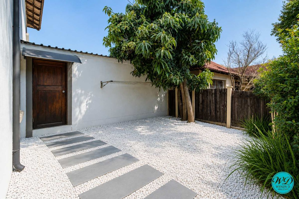 A well-maintained rear courtyard featuring a pebble-covered ground, paved walkway, timber fencing, and a wall-mounted clothesline.