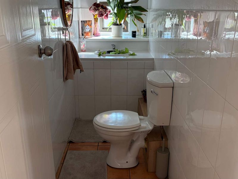 A compact guest bathroom featuring white wall tiles, tiled flooring, a standard toilet, and a small built-in basin area.