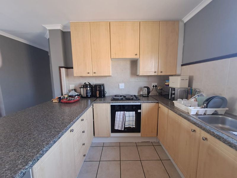 Functional kitchen featuring light wood cabinetry, granite countertops, built-in oven, hob, and tiled flooring, offering a practical layout for daily meal preparation.