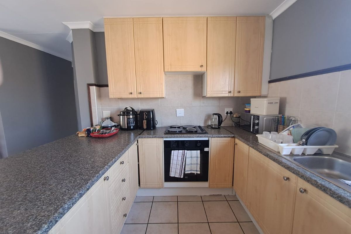 Functional kitchen featuring light wood cabinetry, granite countertops, built-in oven, hob, and tiled flooring, offering a practical layout for daily meal preparation.
